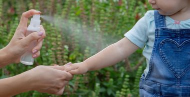 Anne çocuğun vücuduna sprey sprey sıkar. Seçici odak.