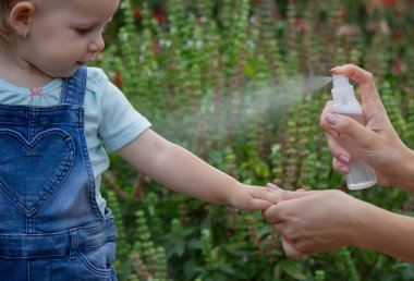 Anne çocuğun vücuduna sprey sprey sıkar. Seçici odak.