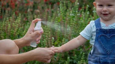 Anne çocuğun vücuduna sprey sprey sıkar. Seçici odak.