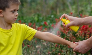 Anne çocuğun vücuduna sprey sprey sıkar. Seçici odak.