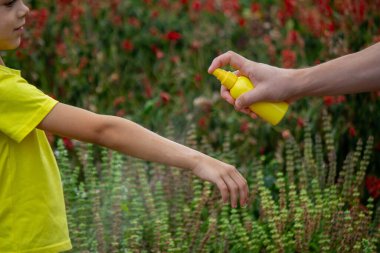 Anne çocuğun vücuduna sprey sprey sıkar. Seçici odak.