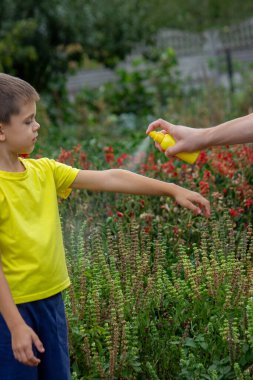 Anne çocuğun vücuduna sprey sprey sıkar. Seçici odak.
