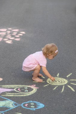 Küçük kız asfalta tebeşirle çiziyor. Seçici odak.