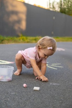 Küçük kız asfalta tebeşirle çiziyor. Seçici odak.