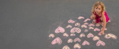 Çocuk asfalta tebeşirle bir kalp çiziyor. Seçici odak.