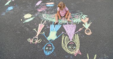 Küçük kız asfalta tebeşirle çiziyor. Seçici odak.