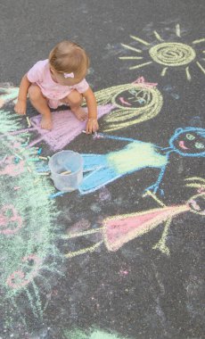 Küçük kız asfalta tebeşirle çiziyor. Seçici odak.