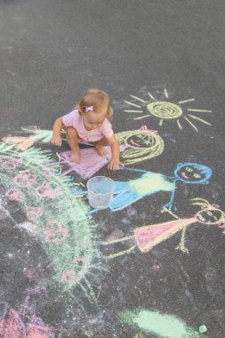 Küçük kız asfalta tebeşirle çiziyor. Seçici odak.