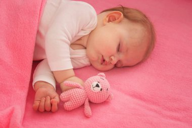 Pembe bir arka planda pembe bir oyuncak ayıyla uyuyan bebek..