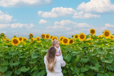 Ayçiçeği tarlasında kucağında küçük bir çocukla güzel bir genç kadın. Bir anne küçük kızına sarılır.