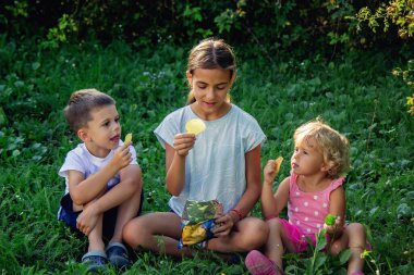 Doğada cips yiyen gülümseyen çocuklar.
