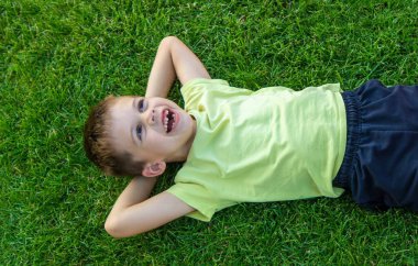 Gülümseyen ve mutlu çocuk yeşil çimlerin üzerinde yatıyor. Çocuklar