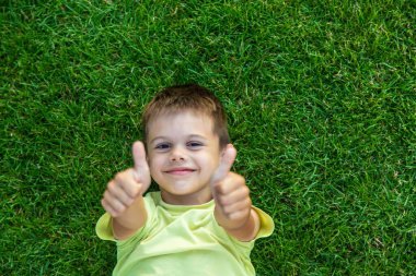 Gülümseyen ve mutlu çocuk yeşil çimlerin üzerinde yatıyor. Çocuklar