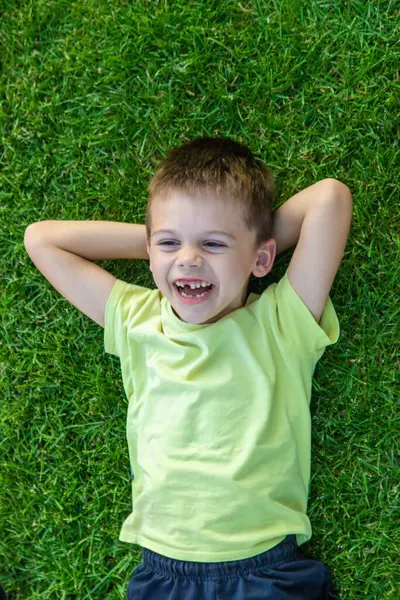 Gülümseyen ve mutlu çocuk yeşil çimlerin üzerinde yatıyor. Çocuklar