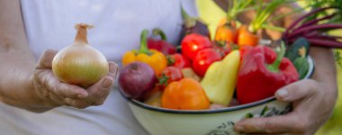 Elinde taze sebze kasesi olan, bahçede hasat yapan bir kadın..