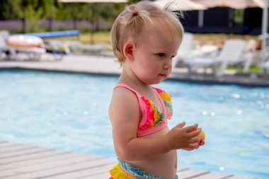 Küçük kız havuzun yanında ve elinde güneş kremi tutuyor. tatil.