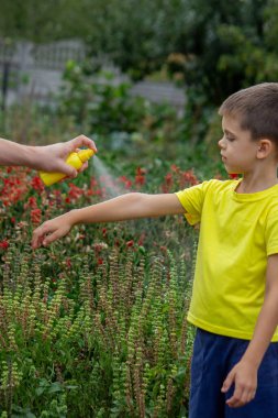 Anne çocuğun vücuduna sprey sprey sıkar. Seçici odak.