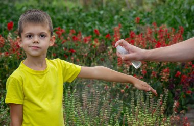 Anne çocuğun vücuduna sprey sprey sıkar. Seçici odak.