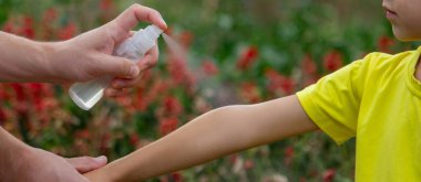 Anne çocuğun vücuduna sprey sprey sıkar. Seçici odak.