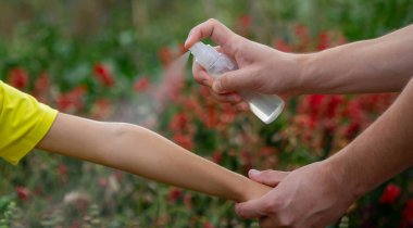 Anne çocuğun vücuduna sprey sprey sıkar. Seçici odak.