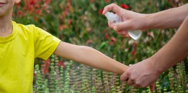 Anne çocuğun vücuduna sprey sprey sıkar. Seçici odak.