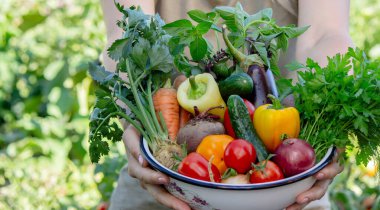 Kadın çiftçi arka planda bir kase sebze tutuyor..