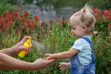Anne çocuğun vücuduna sprey sprey sıkar. Seçici odak.