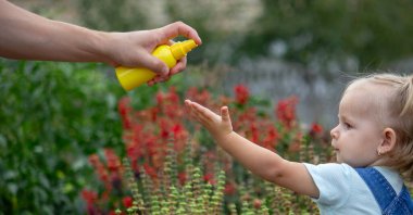 Anne çocuğun vücuduna sprey sprey sıkar. Seçici odak.