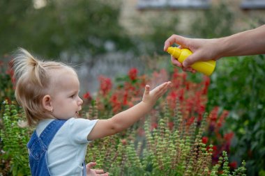 Anne çocuğun vücuduna sprey sprey sıkar. Seçici odak.