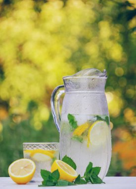 Limonlu bir bardak limonata ve bahçedeki arka planda taze nane şekeri.