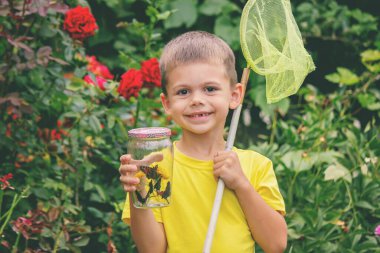 Çocuk bahçede bir kelebek yakalar.