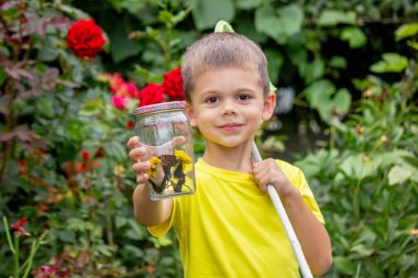 Çocuk bahçede bir kelebek yakalar.