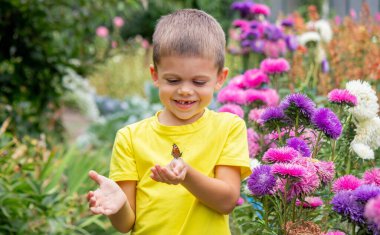 Çocuk bahçede bir kelebek yakalar.