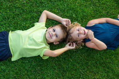 Çocuk yeşil çimlerin üzerinde yatıyor. Çocuk kameraya bakıyor.