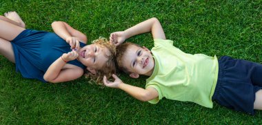 Çocuk yeşil çimlerin üzerinde yatıyor. Çocuk kameraya bakıyor.