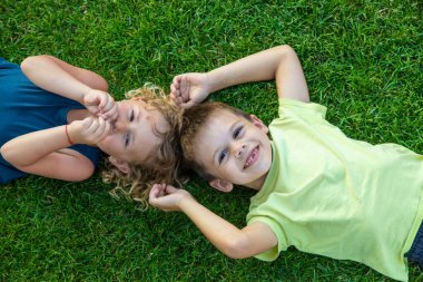 Çocuk yeşil çimlerin üzerinde yatıyor. Çocuk kameraya bakıyor.
