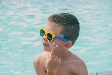 Bir çocuk yüzme havuzunun arka planına güneş kremi sürüyor. Güneş losyonu