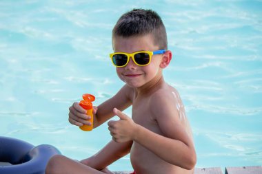 Bir çocuk yüzme havuzunun arka planına güneş kremi sürüyor. Güneş losyonu