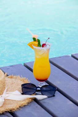 Havuz kenarında güzel bir kokteyl, şapka ve güneş gözlüğü..