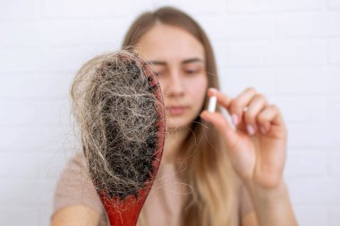 Kadının elinde saç fırçası ve saç dökülmesinden kalma vitaminler var. Seçici odak.