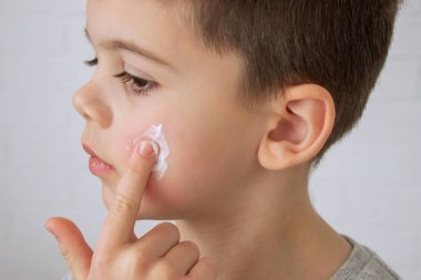 Çocuk kuru cilt için yüzüne krem sürüyor.