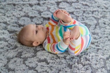Yeni doğmuş bebek ayaklarıyla oynuyor. Evdeki yatakta gökkuşağı renginde güzel bir tulum giyiyor.