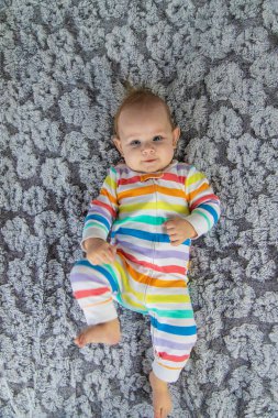 Yeni doğmuş bebek ayaklarıyla oynuyor. Evdeki yatakta gökkuşağı renginde güzel bir tulum giyiyor.