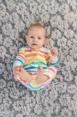 Yeni doğmuş bebek ayaklarıyla oynuyor. Evdeki yatakta gökkuşağı renginde güzel bir tulum giyiyor.