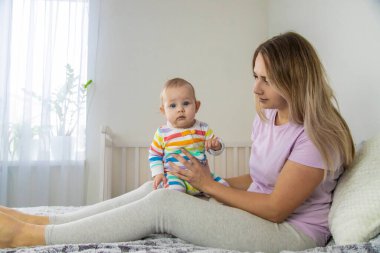 Anne yatakta bebekle oynuyor, bebeğe sarılıyor. Mutlu çocukluk.