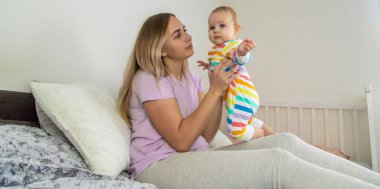 Anne yatakta bebekle oynuyor, bebeğe sarılıyor. Mutlu çocukluk.