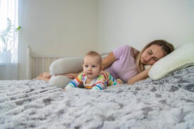 Genç anne uyuyor ve bebek onun yanında yürüyor. Yorgun anne.