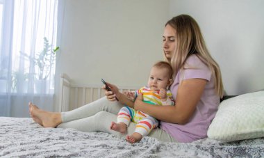 Yavrusu yanındaki yatakta sürünürken genç bir anne telefonuna bakar..