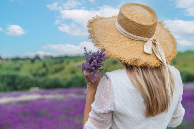 Lavanta tarlasında bir kadın. Beyaz elbiseli ve hasır şapkalı mutlu kadın lavanta tarlasında yürüyor.