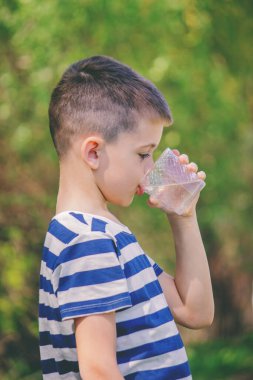 Çocuk arka planda bir bardaktan su içiyor.